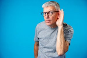 close up of middle age man over blue background with hand over ear listening