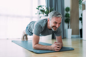 mature man doing plank position while exercising on the floor at home